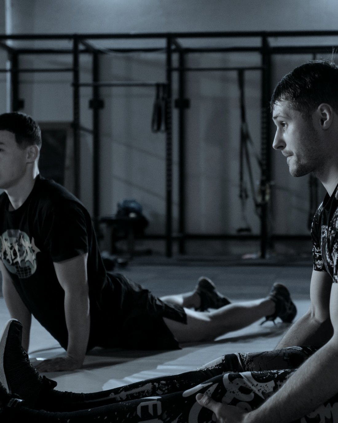 Two men sat on the floor of a gym after training, neither of them talking.